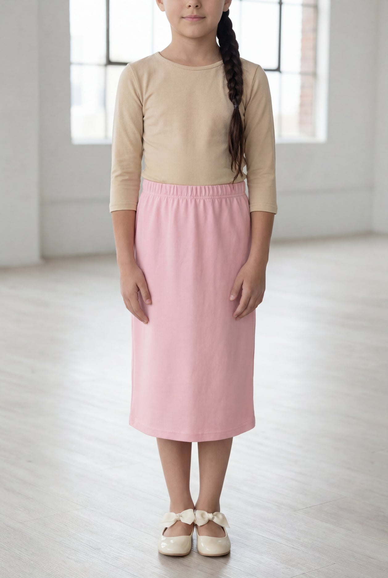 Girl wearing a Nuggles® blush midi length classic skirt with a 3/4 sleeve length soft tee in a sunlight loft. 