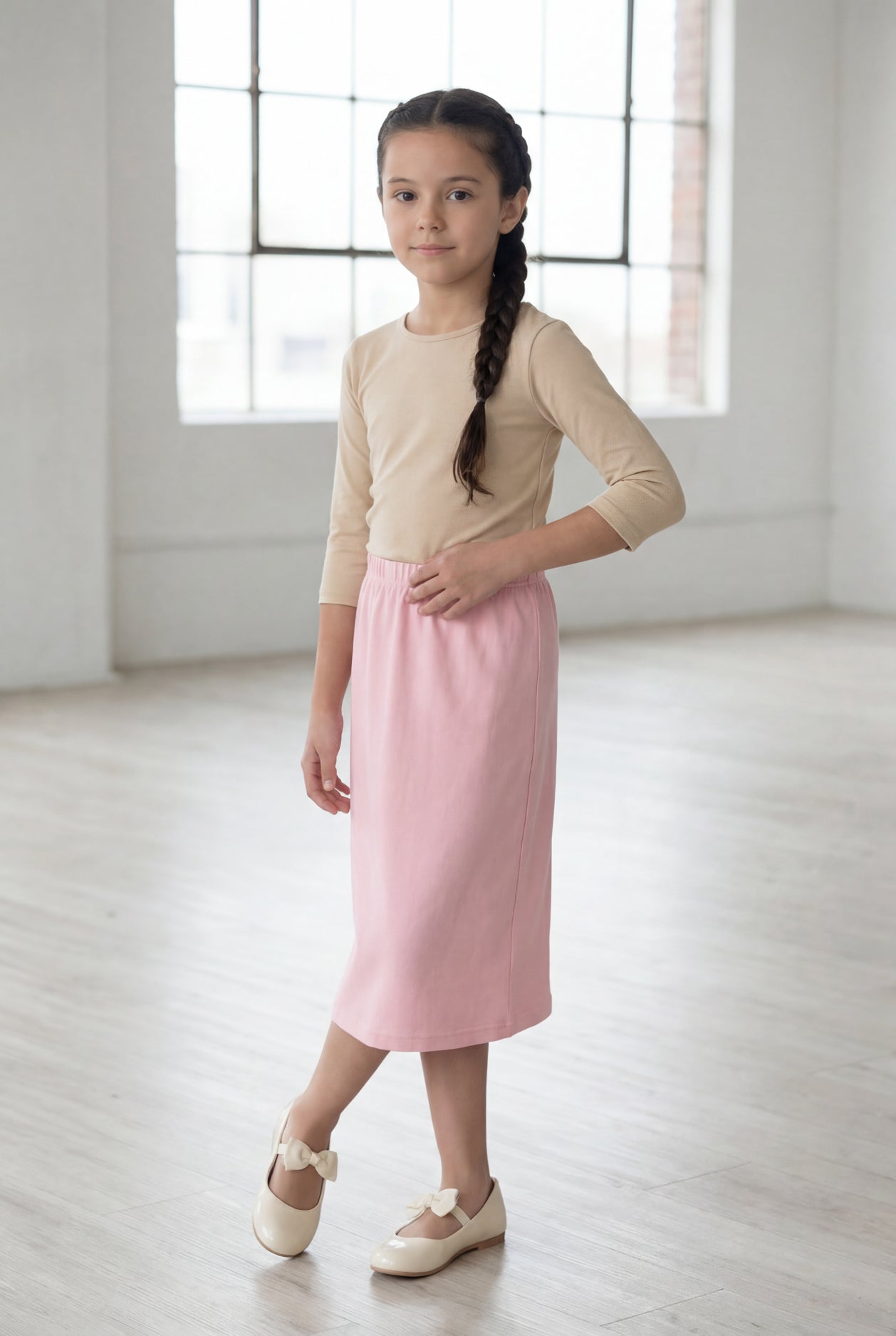 Girl wearing a Nuggles® blush midi length classic skirt with a 3/4 sleeve length soft tee in a sunlight loft. 