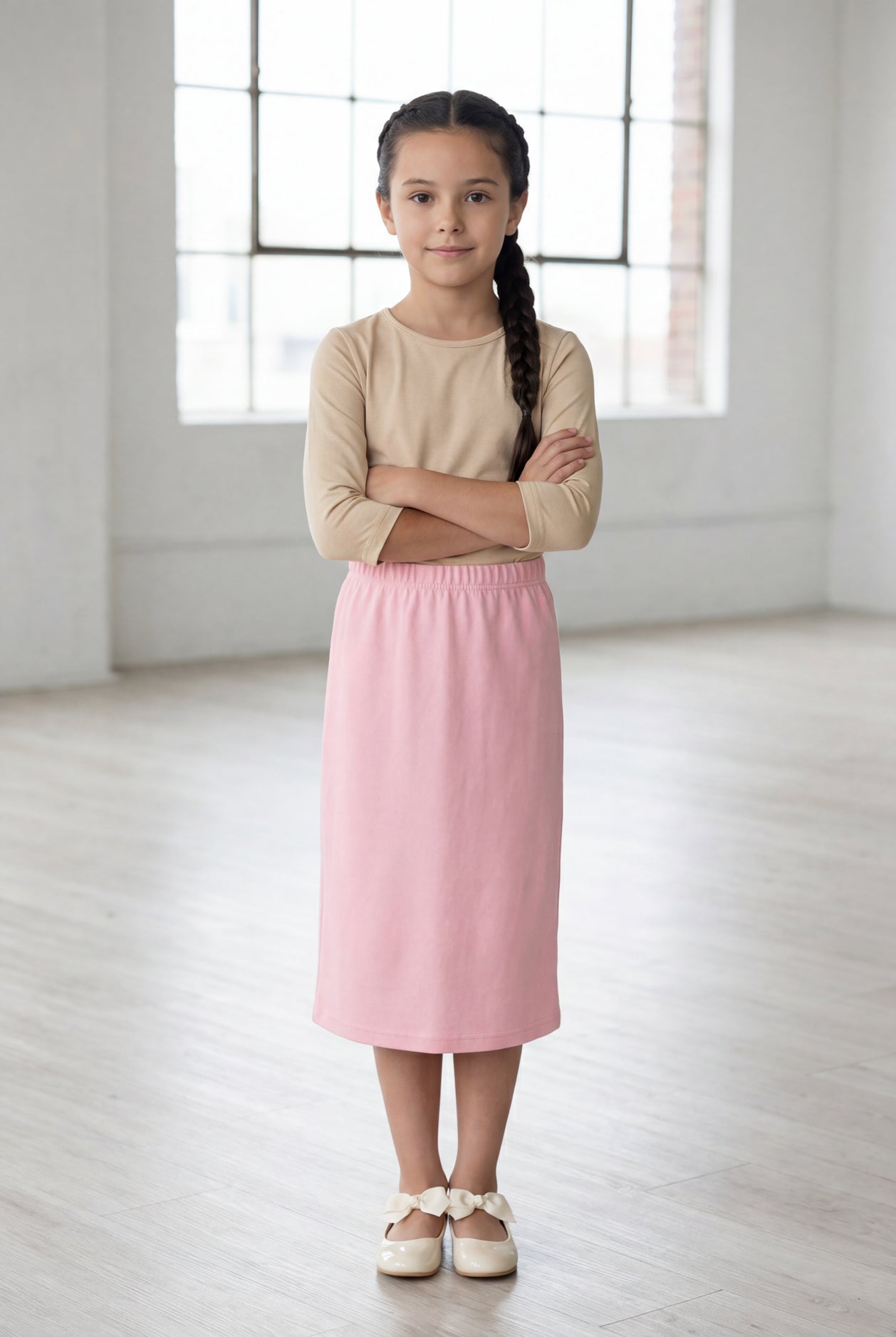 Girl wearing a Nuggles® blush midi length classic skirt with a 3/4 sleeve length soft tee in a sunlight loft. 