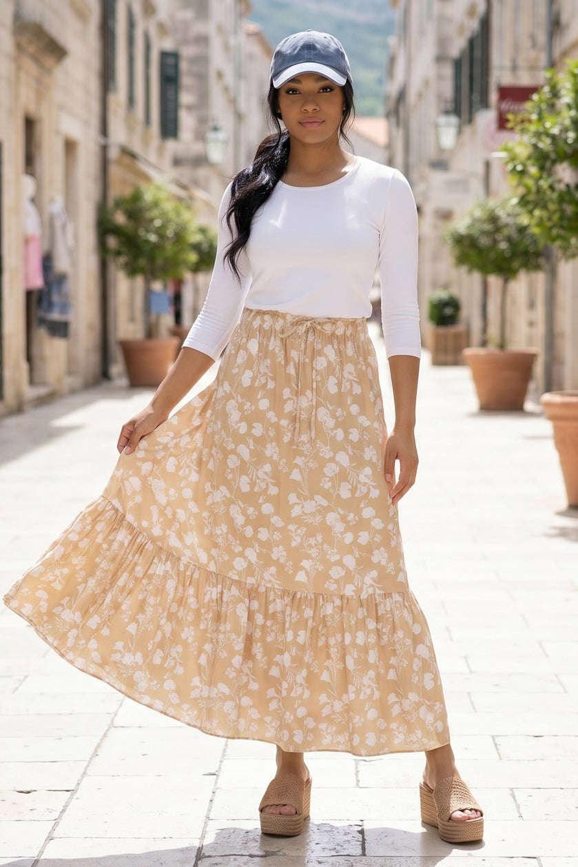 Woman in a white top and beige floral skirt standing on a stone-paved street.