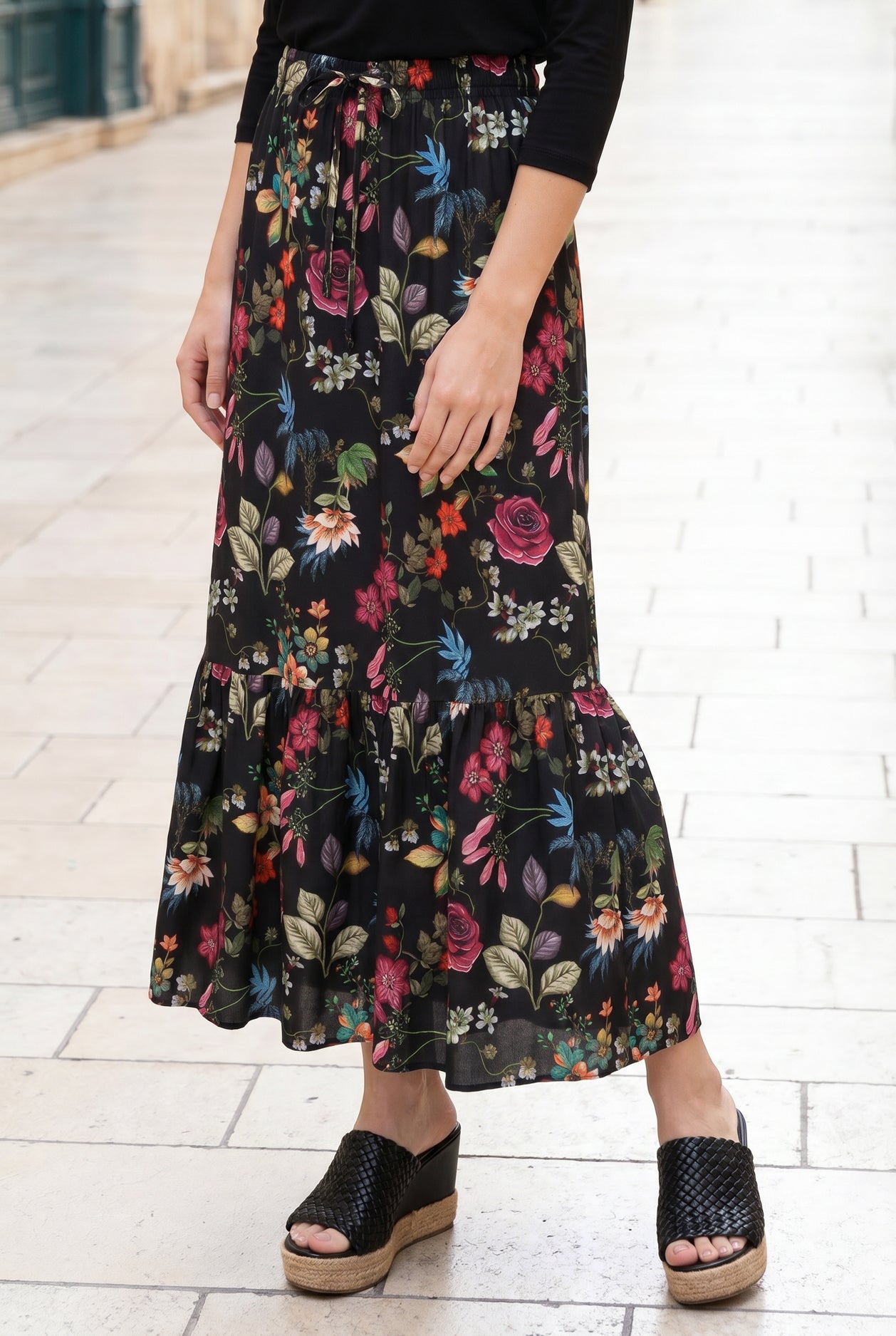 Person wearing a long floral skirt on a white tiled floor.