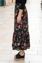Person wearing a black floral skirt on a light stone pavement.