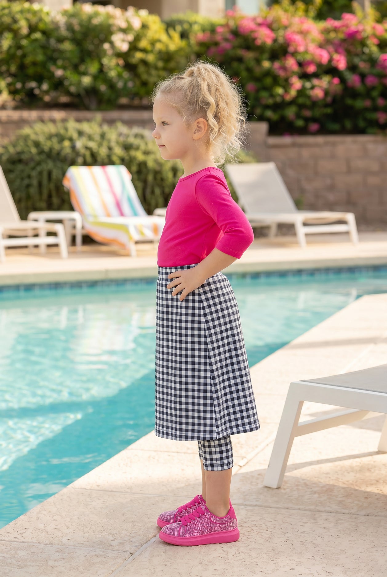 A picture of a young girl beside a pool with a beach ball wearing a modest skort with a coordinating hot pink shirt.