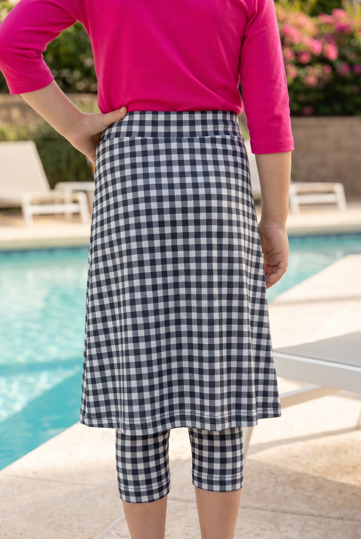 A picture of a young girl beside a pool with a beach ball wearing a modest skort with a coordinating hot pink shirt.