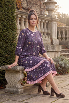 Nuggles® Patricia Dress in Twilight Garden, seated on a stone bench with the tiered skirt draped