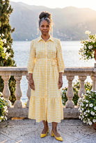 A picture of a women wearing a yellow and white gingham shirt dress with side ties. 