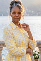 A picture of a women wearing a yellow and white gingham shirt dress with side ties. 