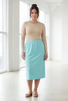 Woman wearing a beige top and light blue skirt in a bright room.