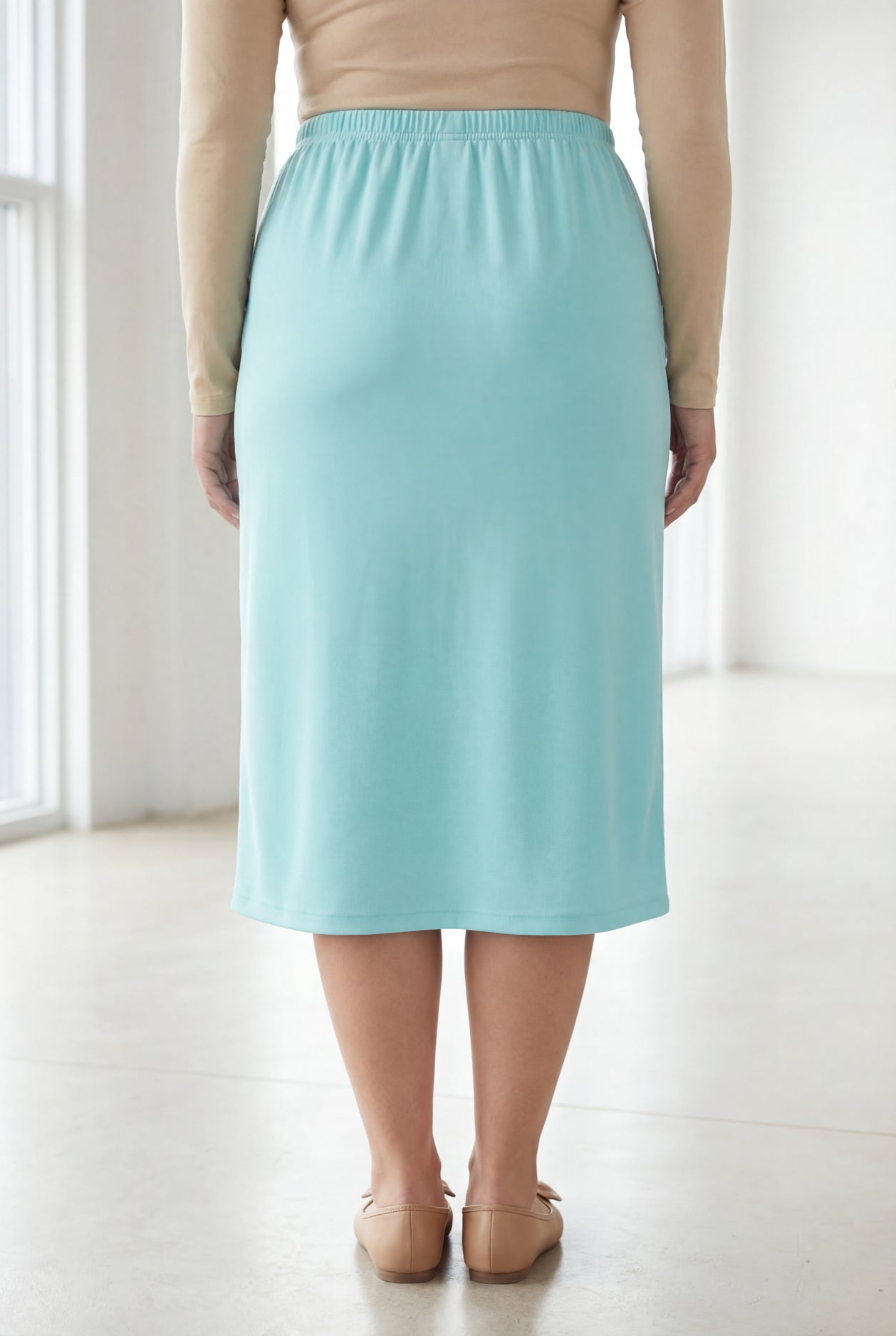 Woman wearing a beige top and light blue skirt in a bright room.