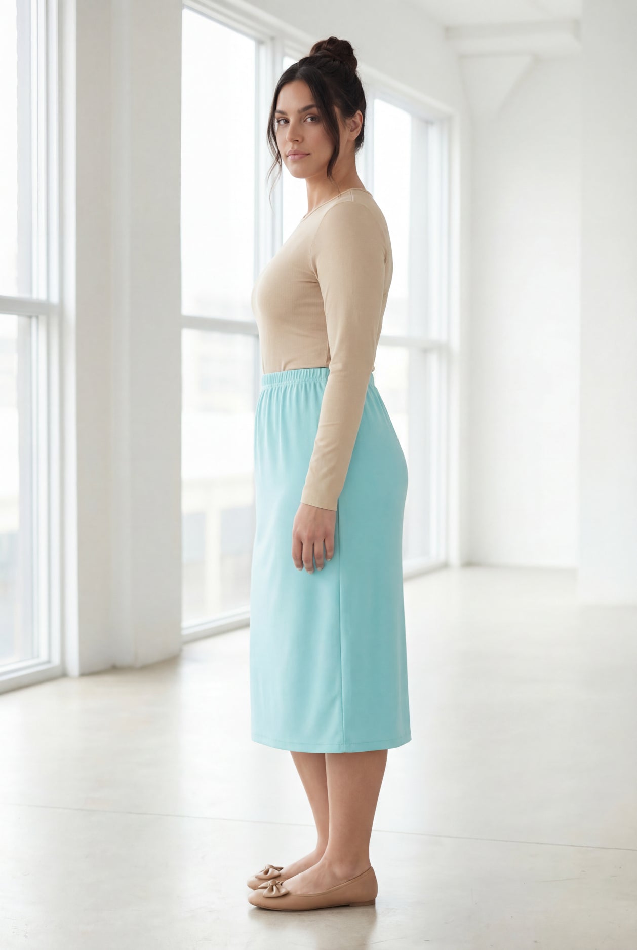 Woman wearing a beige top and light blue skirt in a bright room.