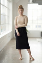 Women wearing a solid black classic 27" midi length skirt with a beige shirt in a sunlight loft.