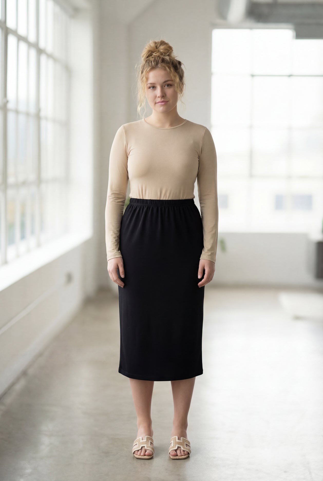 Women wearing a solid black classic 27" midi length skirt with a beige shirt in a sunlight loft.