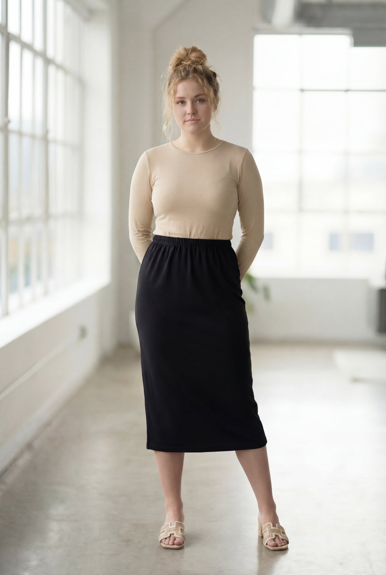 Women wearing a solid black classic 27" midi length skirt with a beige shirt in a sunlight loft.