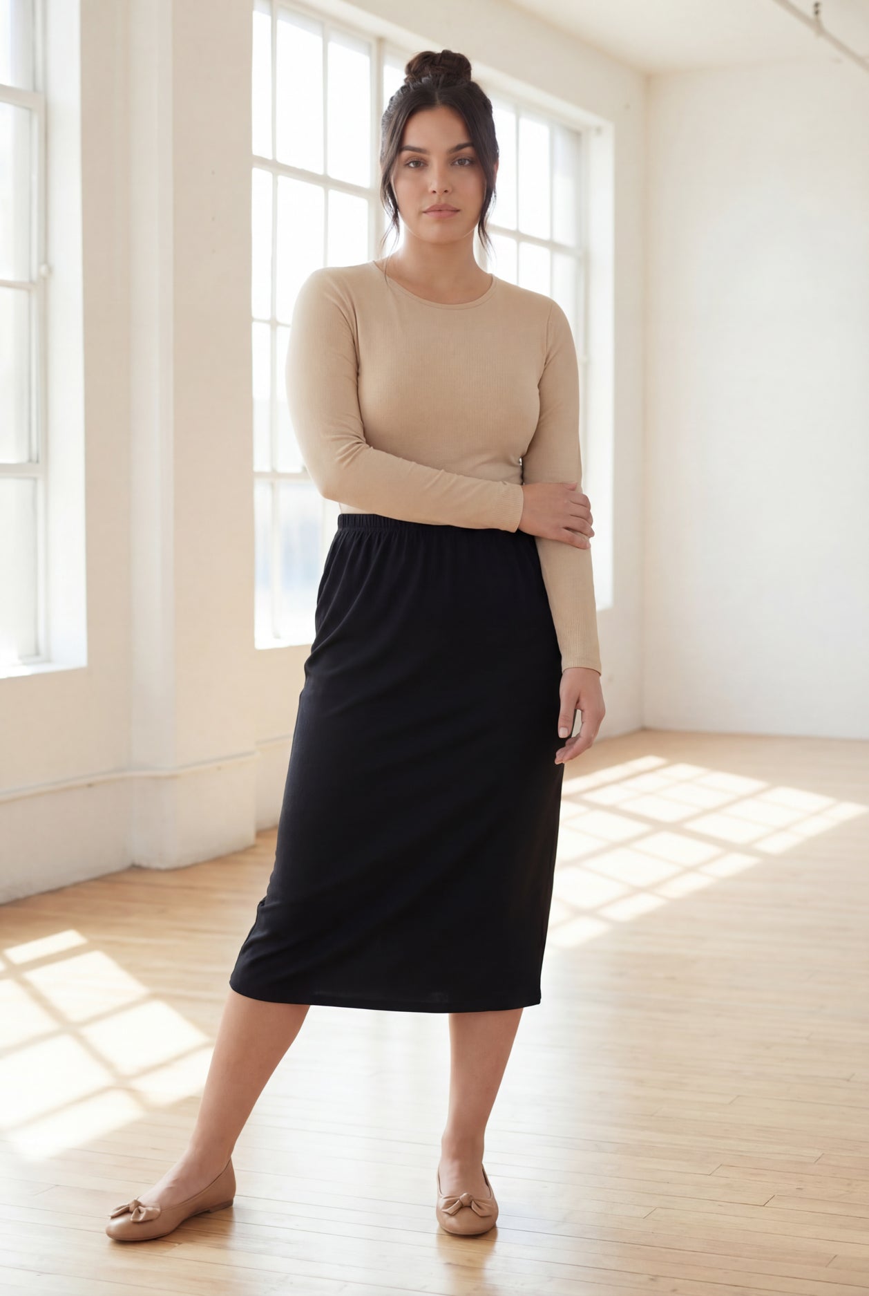 Woman wearing a beige top and  black skirt in a bright room.