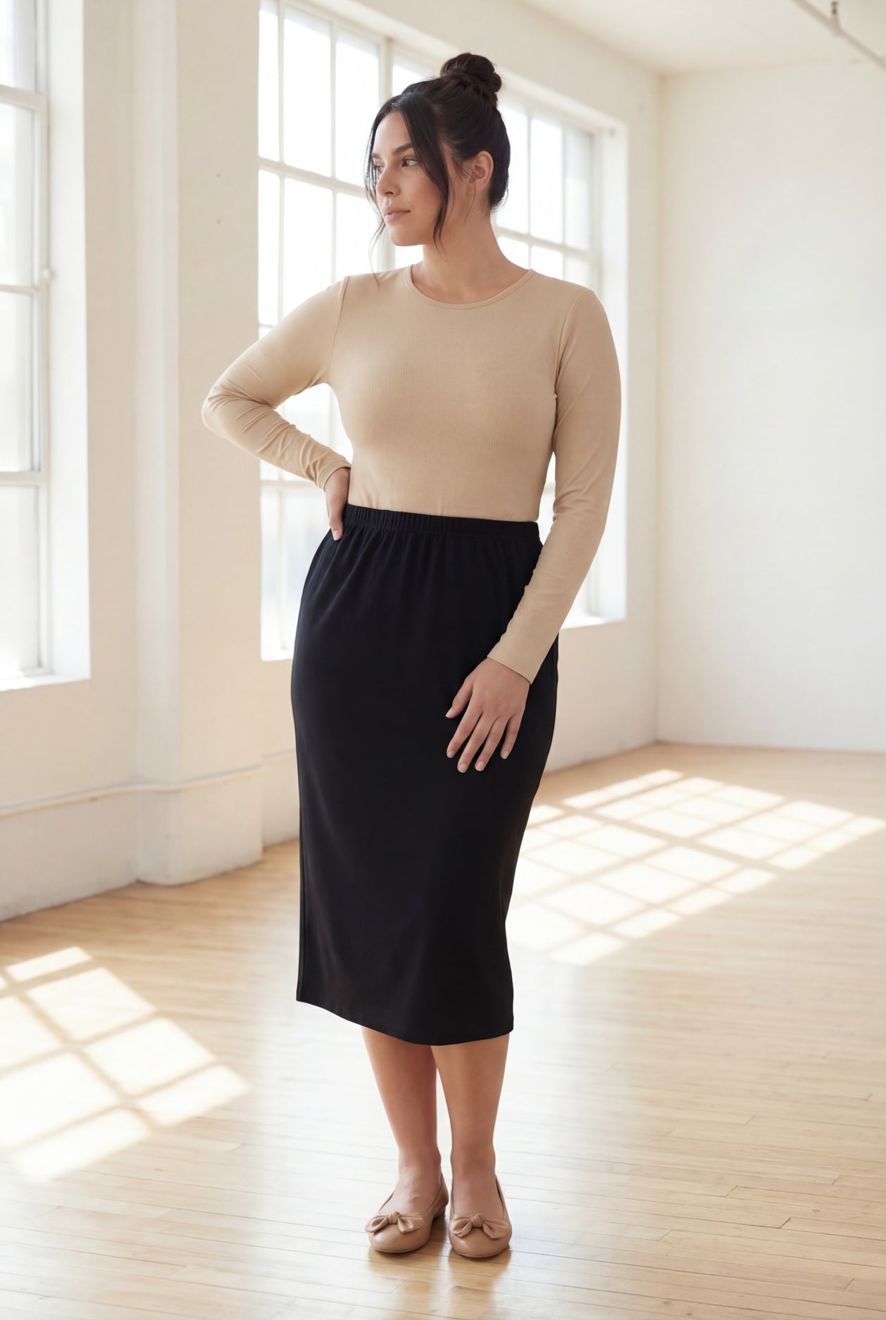 Woman wearing a beige top and  black skirt in a bright room.