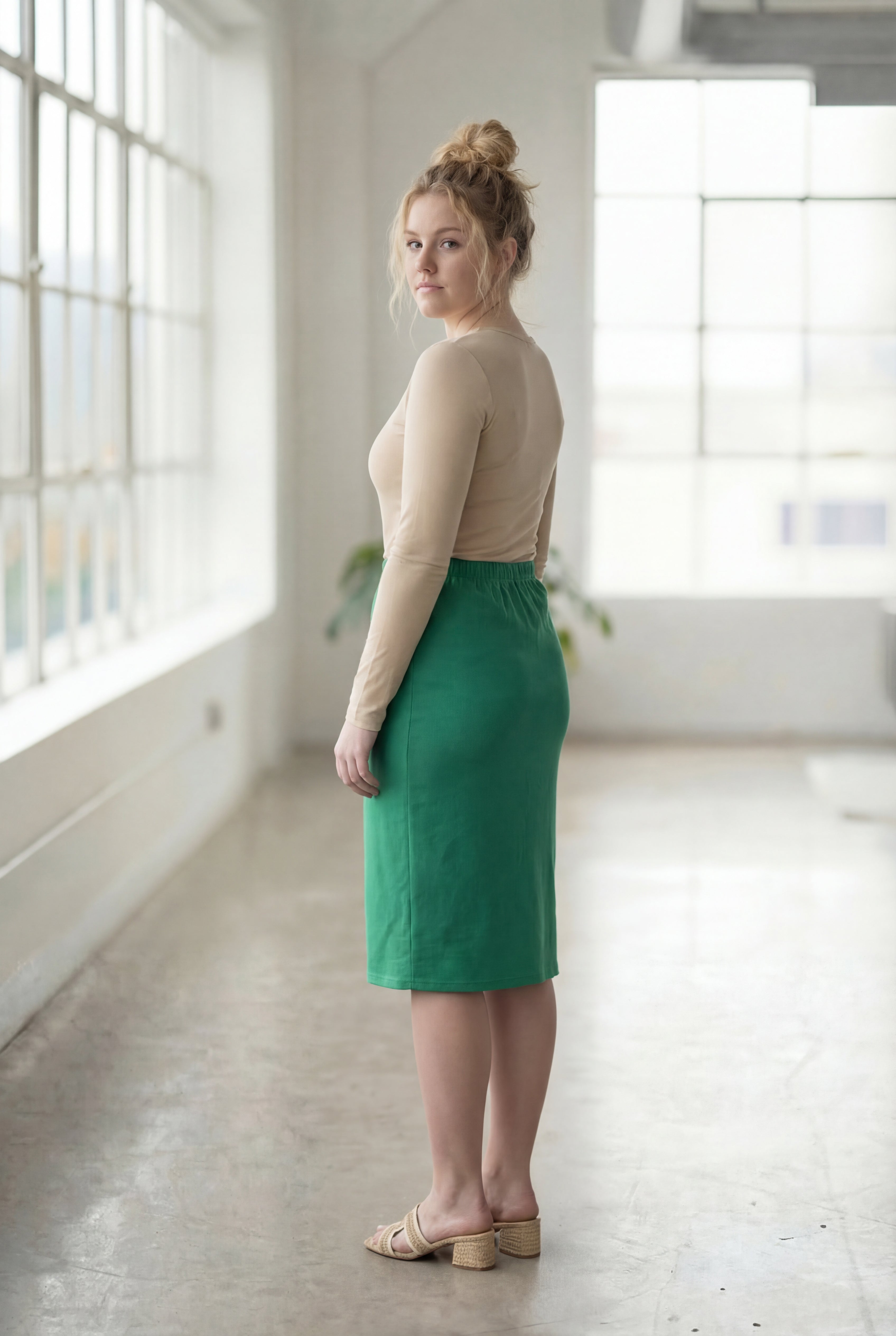 Women wearing a kelly green classic 27" midi length skirt with a beige shirt in a sunlight loft.