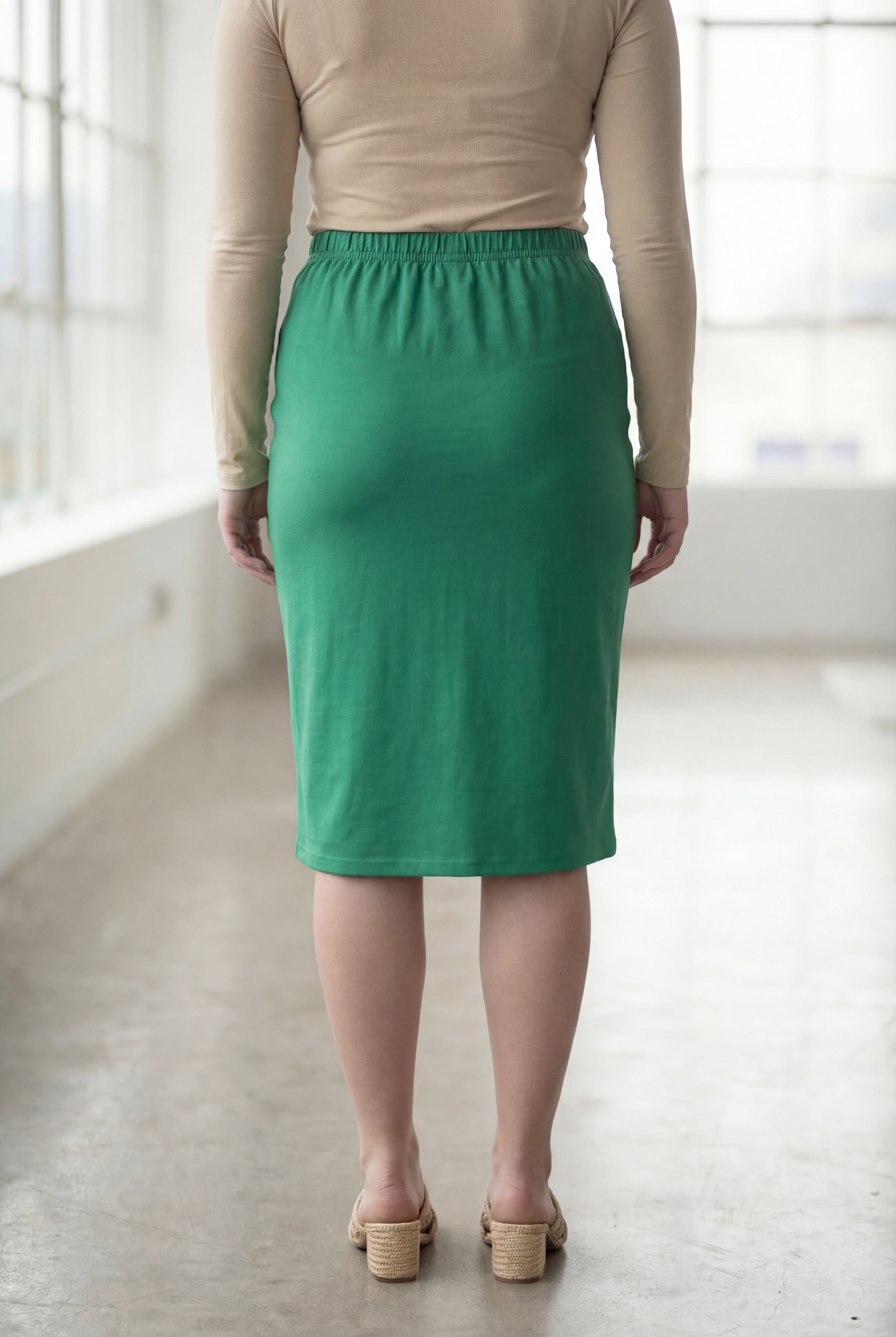 Women wearing a kelly green classic 27" midi length skirt with a beige shirt in a sunlight loft.