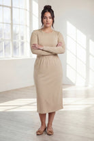 Woman wearing a beige top and beige skirt in a bright room with large windows.