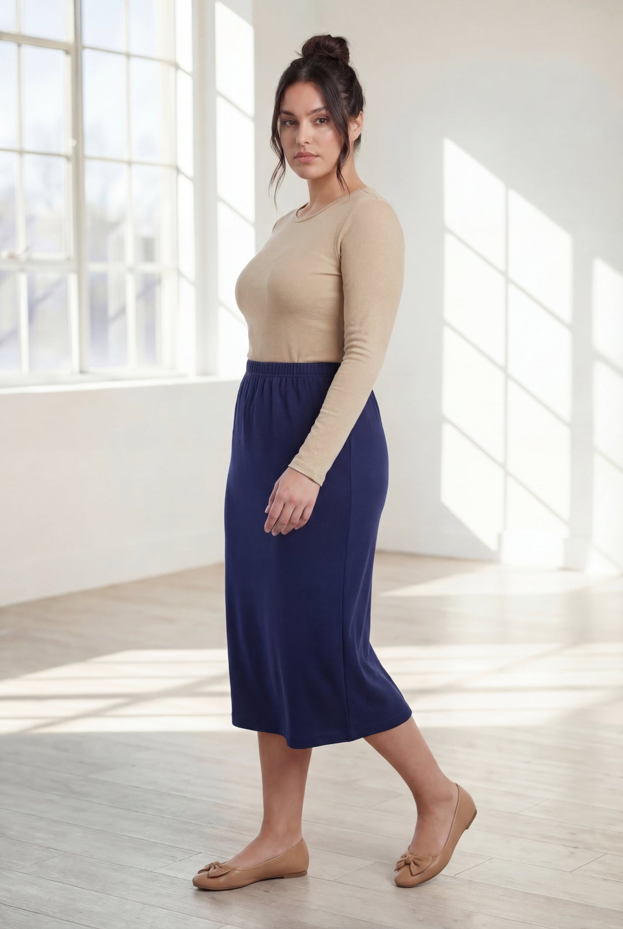 Woman wearing a beige top and  blue skirt in a bright room.