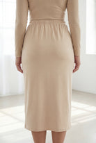 Woman wearing a beige shirt & skirt standing in a bright, minimalistic room.