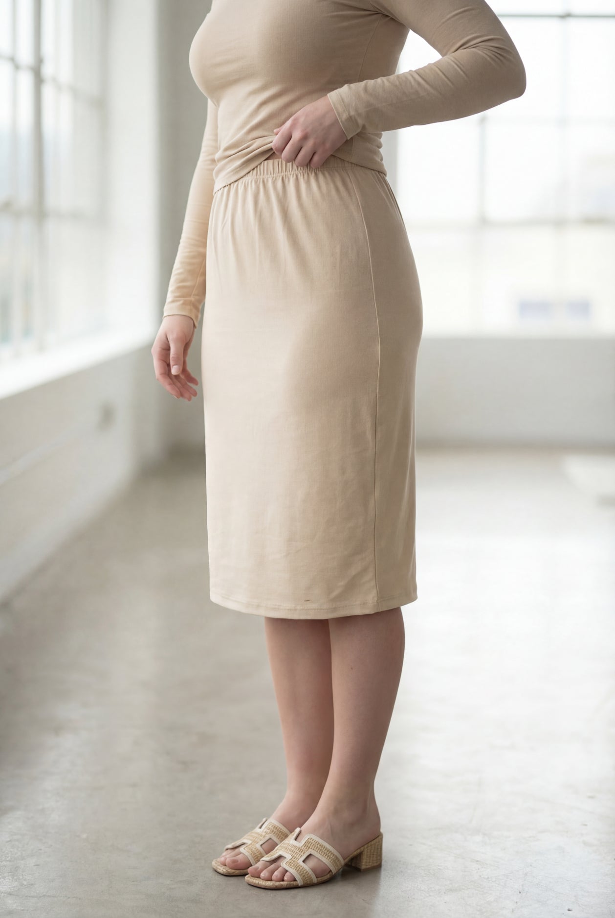 Women wearing a nude classic 27" midi length skirt with a beige shirt in a sunlight loft.