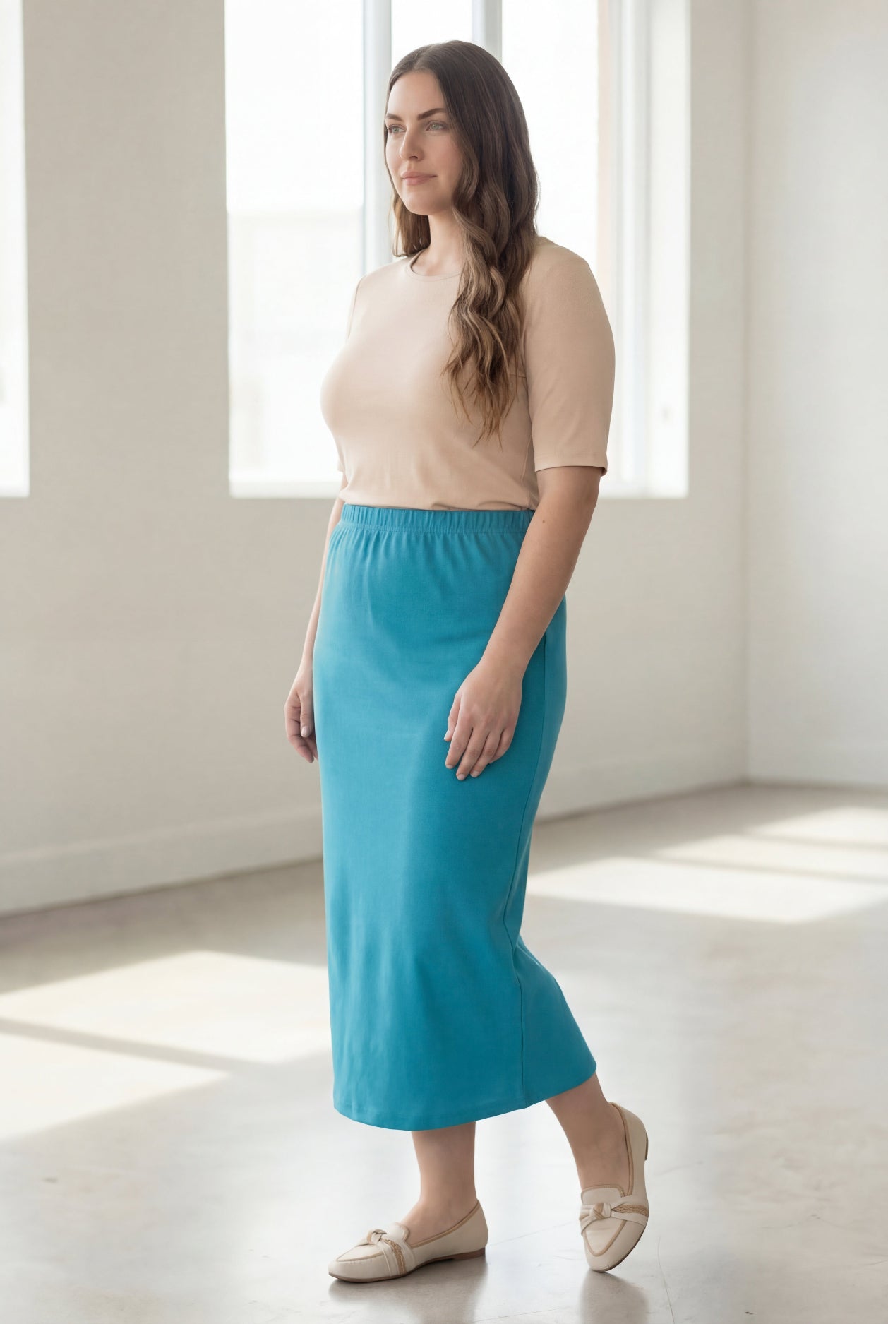 Woman wearing a beige top and blue skirt in a bright room.