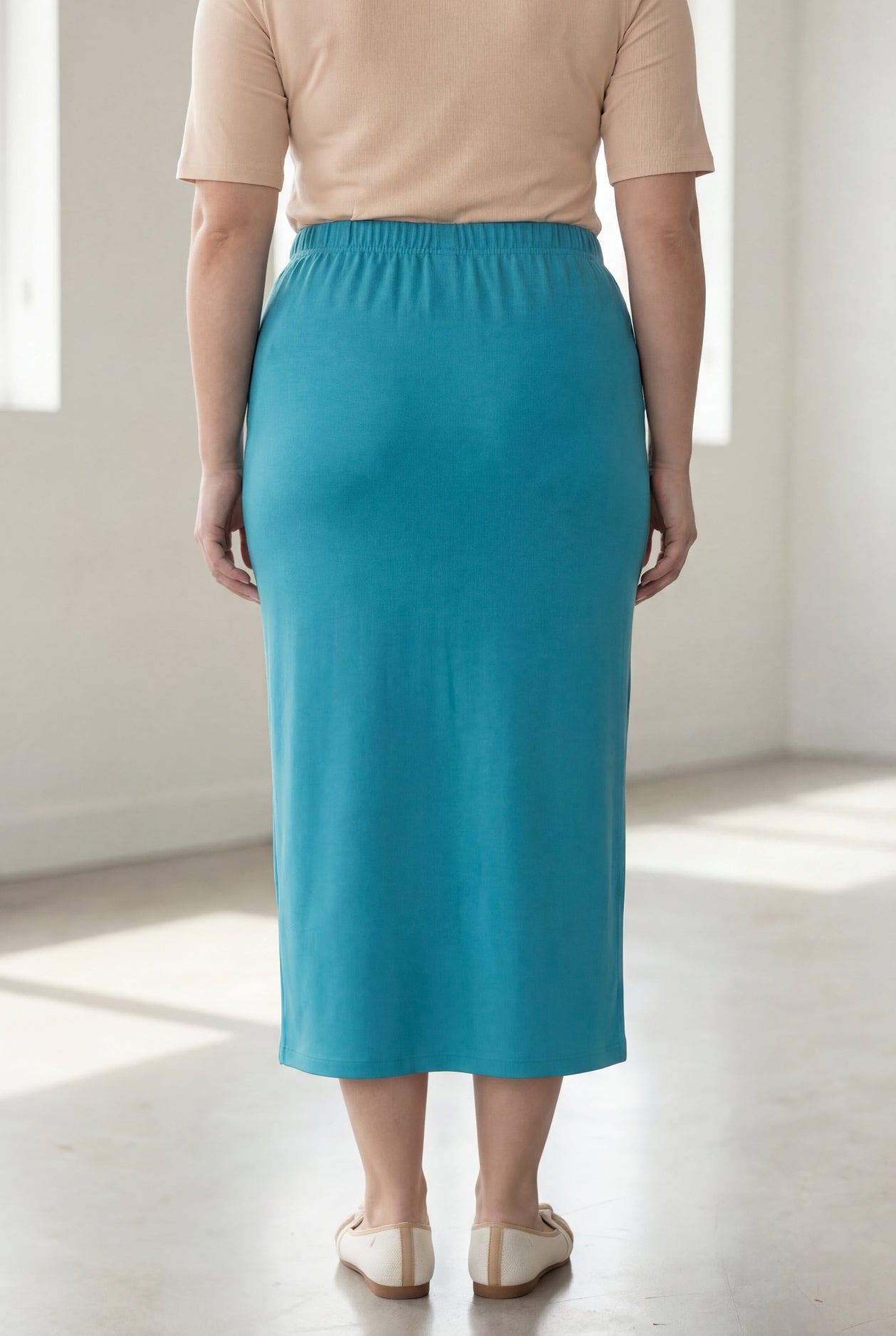 Person wearing a teal skirt and beige top in a bright room